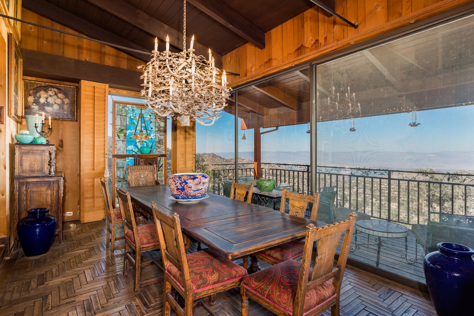 Wood-paneled dining room with stained glass, antler chandelier, and a screened porch overlooking the valley.